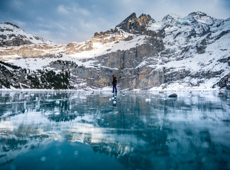 girl in winter outfit looking down on frozen lake Oeschinensee