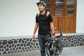 smiling asian young man carrying her folding bike before go in front the house