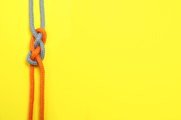 Top view of colorful ropes tied together on yellow background, space for text. Unity concept
