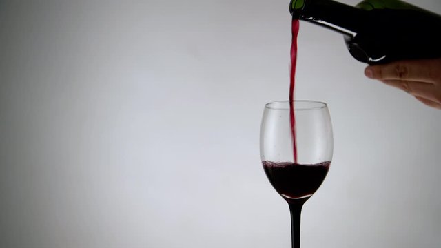 Pouring red wine into a glass on white background. Wineglass full of alcohol drink on light backdrop