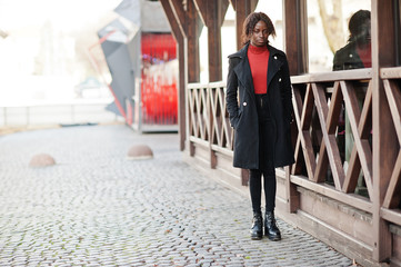 Portrait of a curly haired african woman wearing fashionable black coat and red turtleneck posing outdoor.