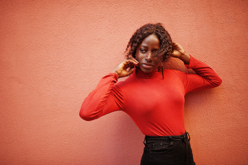 Portrait of a curly haired african woman wearing fashionable red turtleneck posing against rose...