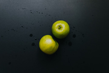 Green apple on black background with water drops, flat lay.