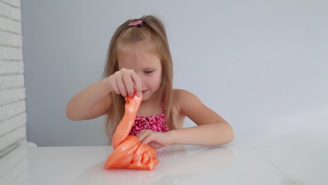 Girl stretching orange slime to the sides. Kids hands playing slime toy on grey background. 