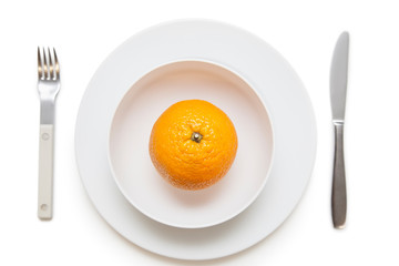 High angle view of an orange in dish with fork and knife over white background