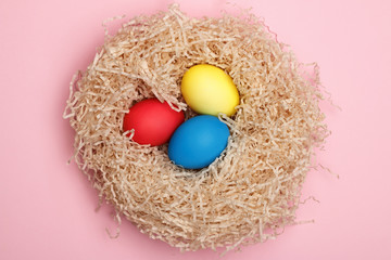 Nest with three easter eggs on a pink background. Close-up. Top view