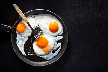 Fried eggs of three eggs in a pan with a fork. Black background