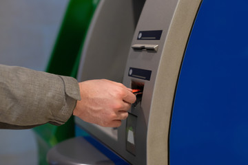 A male hand inserts a credit card into an ATM. Hole for a plastic card. Man withdraws cash through, cashless payment service