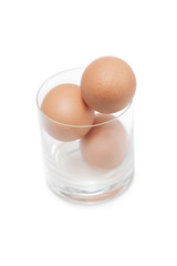 Three brown eggs in drinking glass over white background