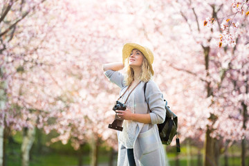 Portrait of a beautiful woman in straw hat traveling in beautiful park with cherry trees in bloom,...