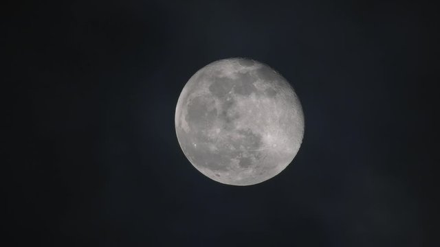 Dark clouds pass moon at night nearly in full phase seen by refractor telescope