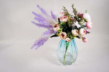A bouquet of roses with lavender in a transparent glass vase on a gray-violet background. Front view