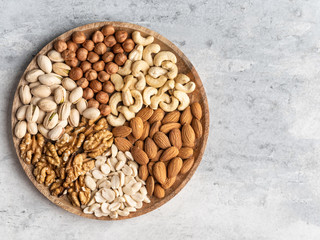 Variety of nuts in wooden plate on grey concrete background. Mixed nuts in wooden bowl. Almond, walnut, peanut, cashew, hazelnut, pistachio. Top view ingredients.