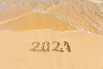 Fototapeta premium New Year 2021 is coming - inscription 2021 on a beach sand, the wave is starting to cover the digits - Summer beach holiday 2021 season golden sand - old year - message handwritten - empty copy space