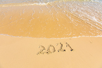 New Year 2021 is coming - inscription 2021 on a beach sand, the wave is starting to cover the digits - Summer beach holiday 2021 season golden sand - old year - message handwritten - empty copy space