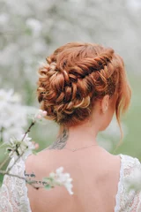 Fotobehang Kapsalon A red-haired woman stands in a flowering spring garden with her back to the camera. Close-up hairstyles.  © MZaitsev