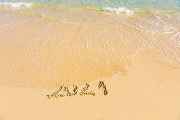 New Year 2021 is coming - inscription 2021 on a beach sand, the wave is starting to cover the digits - Summer beach holiday 2021 season golden sand - old year - message handwritten - empty copy space