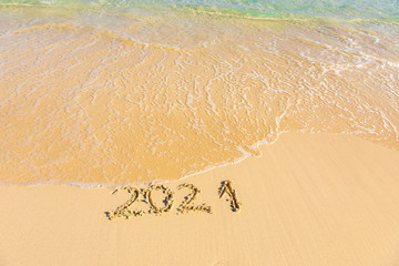 New Year 2021 is coming - inscription 2021 on a beach sand, the wave is starting to cover the digits - Summer beach holiday 2021 season golden sand - old year - message handwritten - empty copy space
