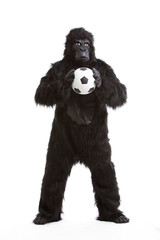 Young man in gorilla costume holding soccer ball against white background