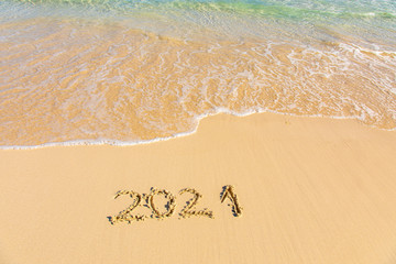 New Year 2021 is coming - inscription 2021 on a beach sand, the wave is starting to cover the digits - Summer beach holiday 2021 season golden sand - old year - message handwritten - empty copy space