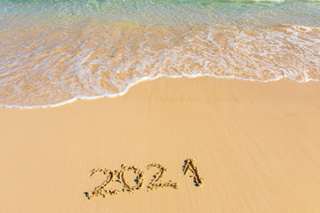 New Year 2021 is coming - inscription 2021 on a beach sand, the wave is starting to cover the digits - Summer beach holiday 2021 season golden sand - old year - message handwritten - empty copy space