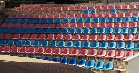Empty auditorium in the open. Semicircular plastic chairs are arranged in rows from bottom to top.  Colorful theater background.