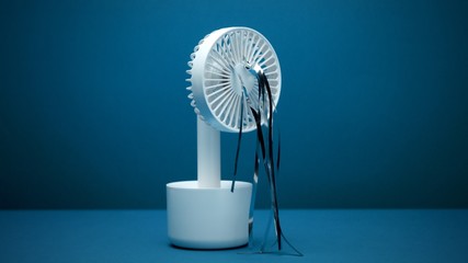 Closeup of switched off small white ventilator with silver strips blowing on deep blue background