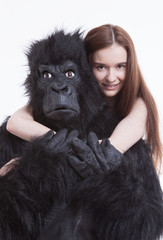 Portrait of smiling young woman hugging man in gorilla costume against white background © MDBPIXS