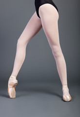 Low section of young ballet dancer wearing standing over grey background © MDBPIXS