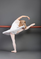 Fototapeta premium Young female ballet dancer stretching at ballet bar over grey background