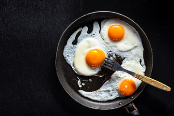 Fried eggs of three eggs in a pan with a fork. Black background