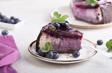 Slice of Blueberry flavour cheesecake swirled with blueberry sauce on a  biscuit crumb, bakery. Delicious slice of blueberries cheesecake with  jam and green mint.  Sweet and tasty food, coffee break 