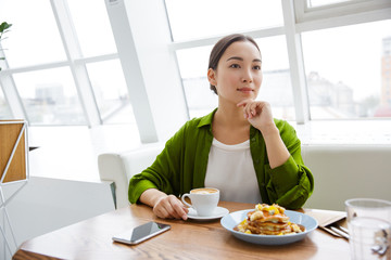 Smiling asian woman having pancakes for breakfast