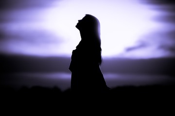 Youth woman soul at purple sun meditation dreaming past times. Silhouette in front of sunset or...