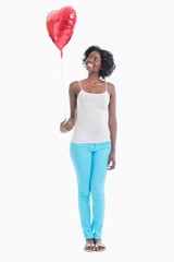 Happy young woman looking at heart shaped balloon over white background