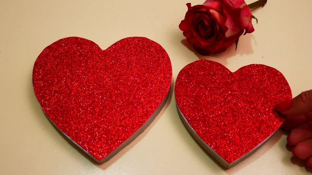 Two bright red shiny hearts and a scarlet rose on a white background. The concept of romantic love, recognition and Valentine's Day.