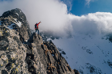 An alpinist standing on top of a high rock and watching winter mountain alpine landscape. Hiker or...