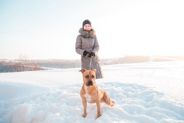 a girl walks her dog in winter. dog staff on a walk in the winter. a pit bull is walking on a chain in the winter. walking on a winter day with a pet