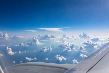 Fototapeta na wymiar Airplane wing above fluffy white clouds in a blue sky.