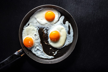 Fried eggs of three eggs in a pan. Black background