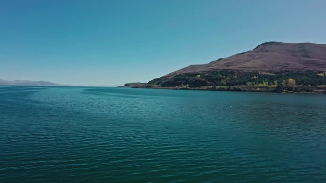 Aerial drone shot pan shot circular of Lake Sevan and seagulls flying on background of Mount Ararat. Aerial drone circular shot of Lake Sevan under bright blue sky