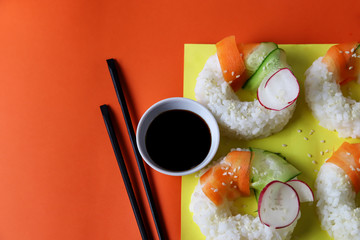 Sushi donuts with raw carrots, cucumber and radish on yellow orange paper background. Contemporary food concept, trendy Asian dinner for vegan or vegetarian, close up, top view
