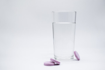 Transparent glass glass with clean water, next to which are soluble. instant or dissolve pink tablets vitamin C, dietary supplements, painkillers