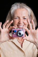 Smiling senior woman taking picture with camera against black background