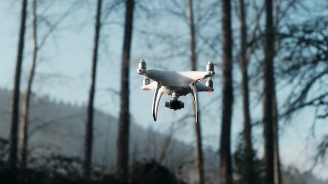 DJI Phantom Four Drone flying in place while slowly turning with trees and hills in the background