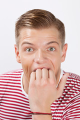 Portrait of amazed young man biting his finger over white background
