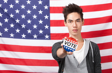 Portrait of young man showing vote badge standing against American flag