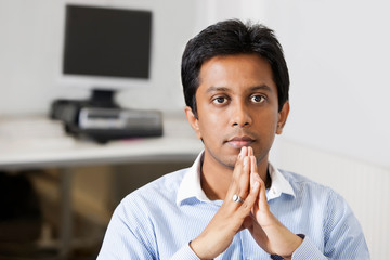 Fototapeta na wymiar Portrait of young pensive businessman with hands clasped sitting at office