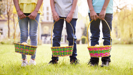 Close Up Of Three Children Holding Baskets On Easter Egg Hunt In Garden