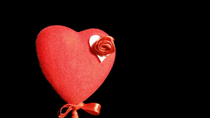 A red heart on a stick with a small red bow, decorated with a small red rose on a white background, emerging from the darkness. Saint Valentine's Day concept. 